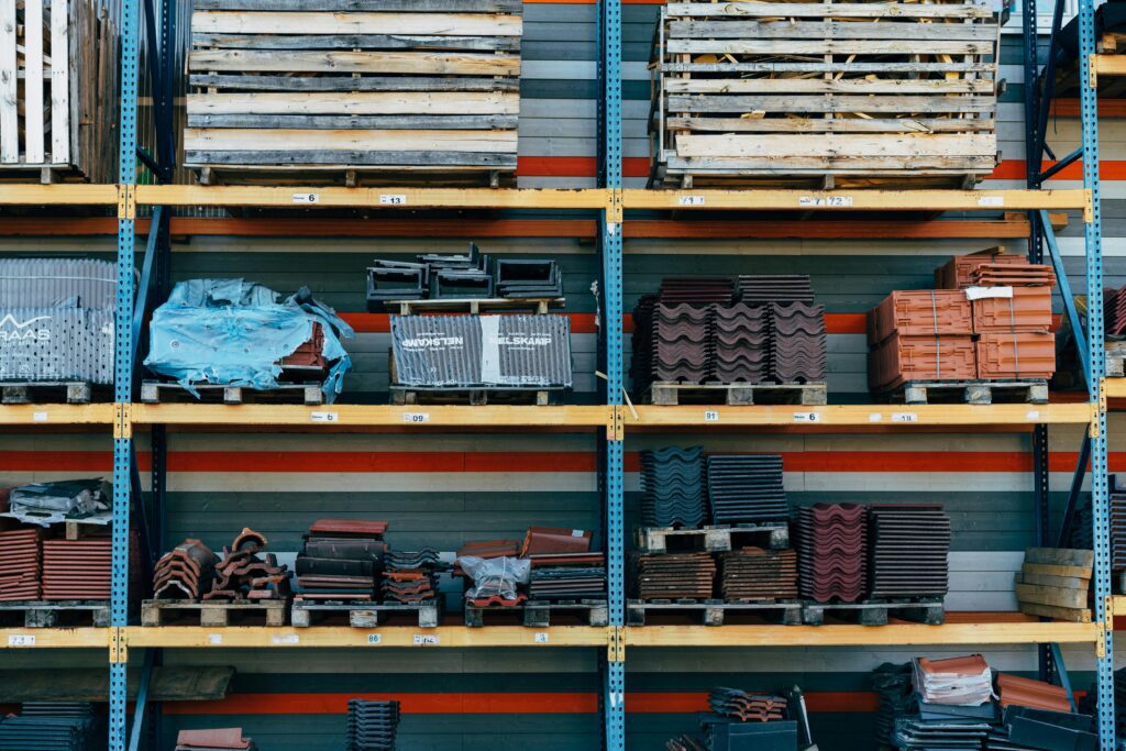 Shelves filled with construction materials like tiles and wood pallets in a warehouse setting.